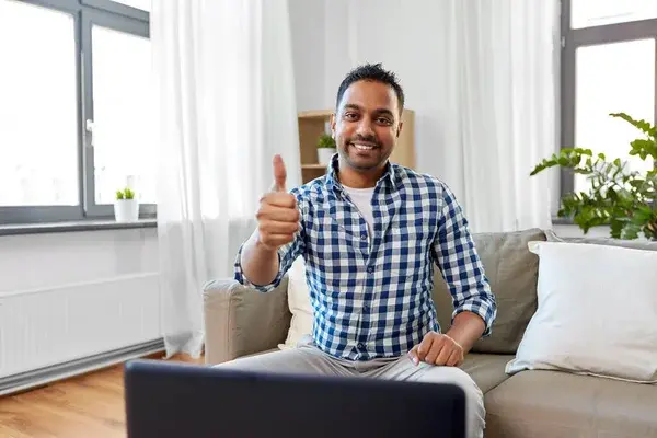 hombre en su casa trabajando desde su computadora enseñando un gesto con su mano