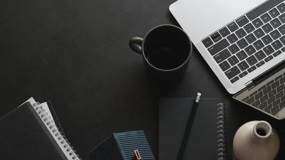 Escritorio de trabajo con computadora, cuaderno, lápiz y taza de café, ideal para planificar temas de contabilidad para emprendedores
